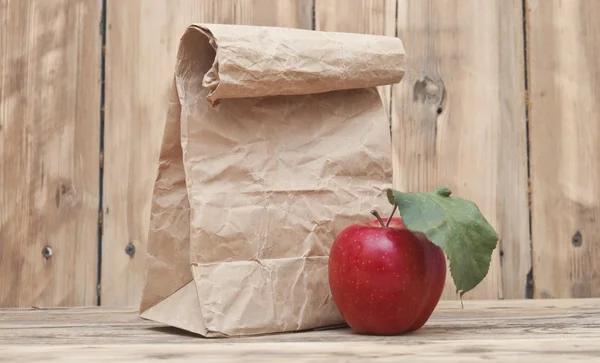 Apfel mit Papiertüte auf einem hölzernen Hintergrund — Stockfoto
