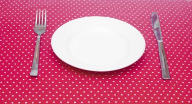 Boş beyaz yemek tabağı ile mutfak eşyaları üzerinde eğlenceli kırmızı puantiyeli tabl