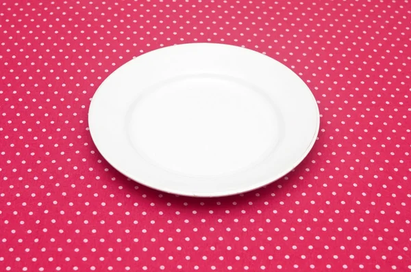 Порожня біла тарілка на веселій червоній точковій скатертині . — стокове фото