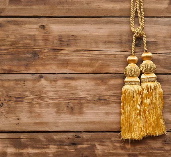 Corda de ouro com borla contra parede de madeira — Fotografia de Stock