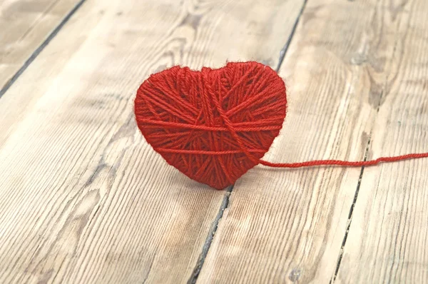 Ahşap arka plan üzerinde kırmızı yün iplik yapılan kalp — Stok fotoğraf