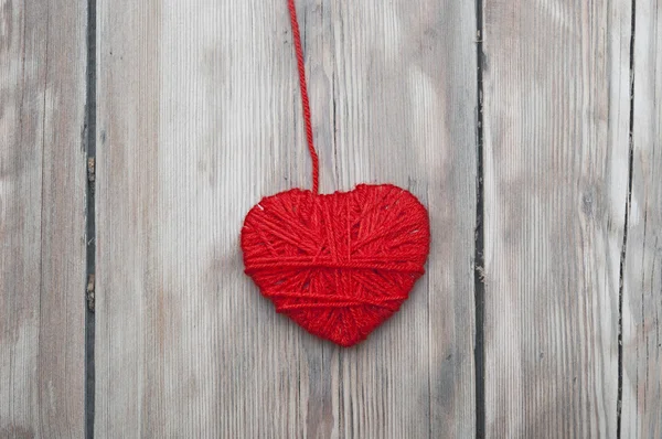 由红色的羊毛纱线制成旧木背景上挂着一颗心. — 图库照片