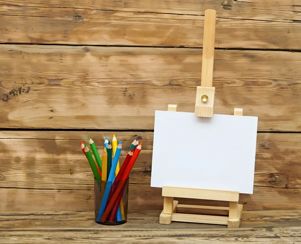 Wooden easel with clean paper and colorful pencils — Stock Photo, Image