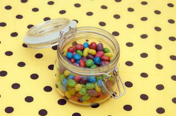 Colorful candies in glass jar on polka dot napkin — Stock Photo, Image