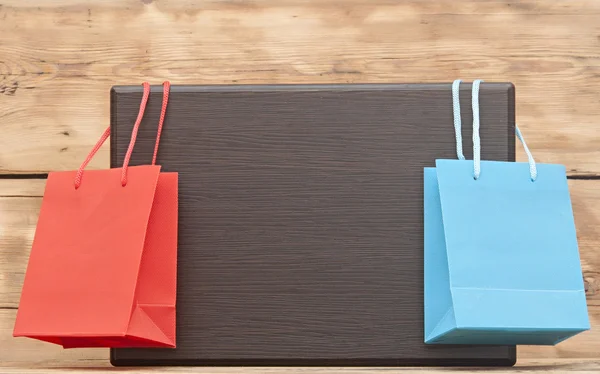 Farbenfrohe Einkaufstaschen hängen auf einem leeren Holzteller mit Kopierplatz für Ihren Text — Stockfoto