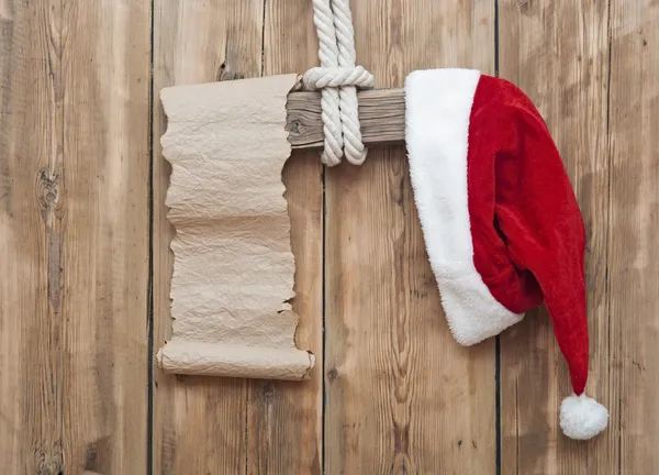 Signo de madera con sombrero de Santa Claus y pergamino de papel en blanco sobre una madera —  Fotos de Stock