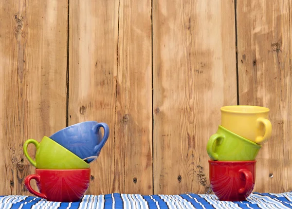 Bunte Kaffeetassen auf gestreifter Tischdecke über Holzhintergrund — Stockfoto