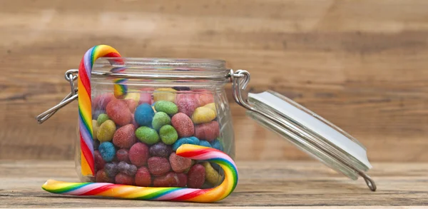 Dulces caramelos de azúcar en frascos de vidrio sobre fondo de madera —  Fotos de Stock