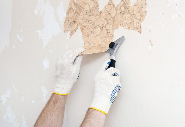 Hand removing wallpaper from wall