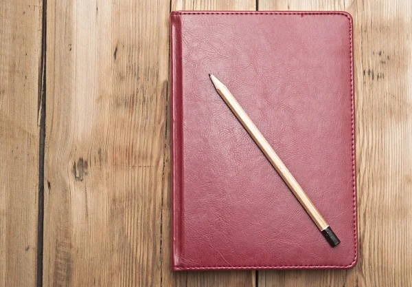 Livro de notas de couro vermelho com lápis sobre fundo de madeira — Fotografia de Stock