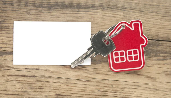 Klíč s ikonu domečku a prázdný papír na dřevěné pozadí — Stock fotografie