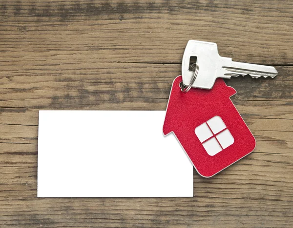 Key with house icon and blank paper on wooden background — Stock Photo, Image