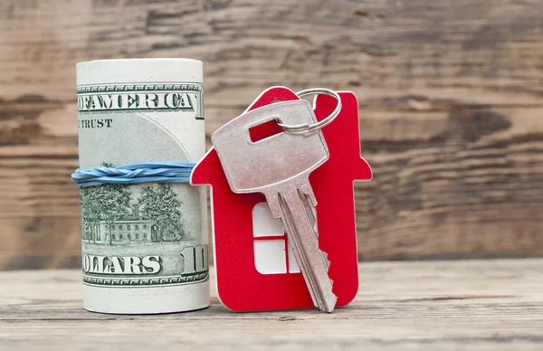 Huis sleutels over de honderd dollar biljetten tegen houten rug — Stockfoto