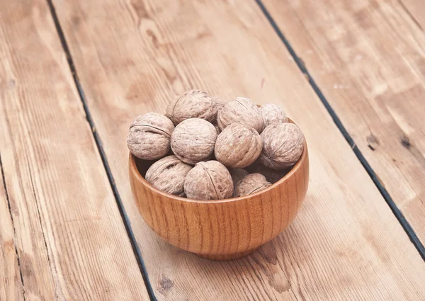 Hela valnötter ligger på bleka trä med ytterligare en nuts i trä — Stockfoto