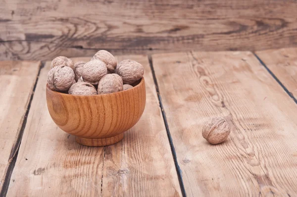 Hela valnötter ligger på bleka trä med ytterligare en nuts i trä — Stockfoto