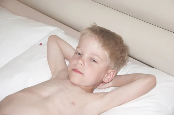 Adorable divertido niño rubio somnoliento acostado en una cama — Foto de Stock