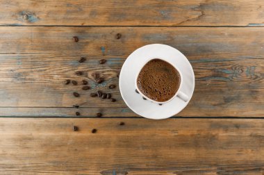 Eski ahşap masada bir fincan kahve ve kavrulmuş fasulye.