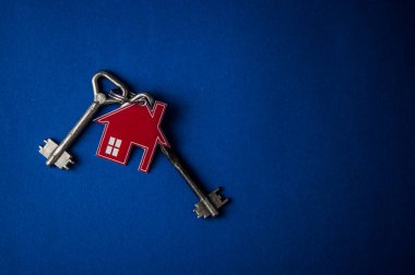 Anahtar ve ev şekilli anahtarlık düzeni mavi arka planda. Üst manzara, düz yatış. Gayrimenkul, sigorta konsepti, ipotek, satış evi, emlakçı konsepti Kopyalama alanı