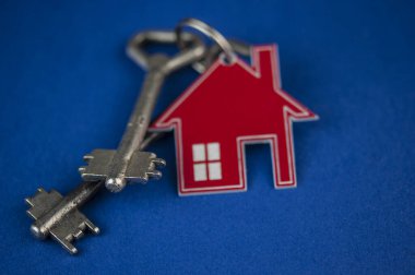 Anahtar ve ev şekilli anahtarlık düzeni mavi arka planda. Üst manzara, düz yatış. Gayrimenkul, sigorta konsepti, ipotek, satış evi, emlakçı konsepti Kopyalama alanı