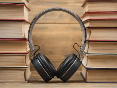 Masada siyah kulaklıklar ve boş renkli kapaklı farklı renkte ciltli kitap yığını. Eskiye karşı yeni. Kapat, kopyala boşluk, arkaplan.