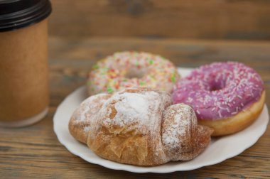 Tahta masaya serpiştirilmiş lezzetli çörekler ve kağıt bardak.