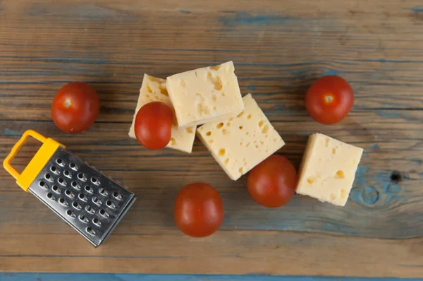 スタックチーズキューブと木製のキッチンテーブルの上にミニチュアグレーターとチェリートマト — ストック写真