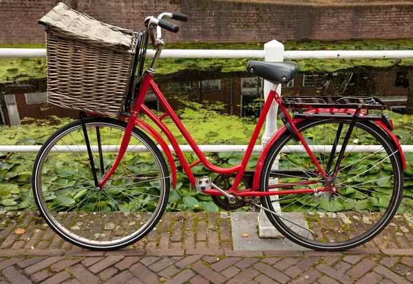 Czerwony rower z koszykiem zaparkowany obok kanału w Holandii — Zdjęcie stockowe