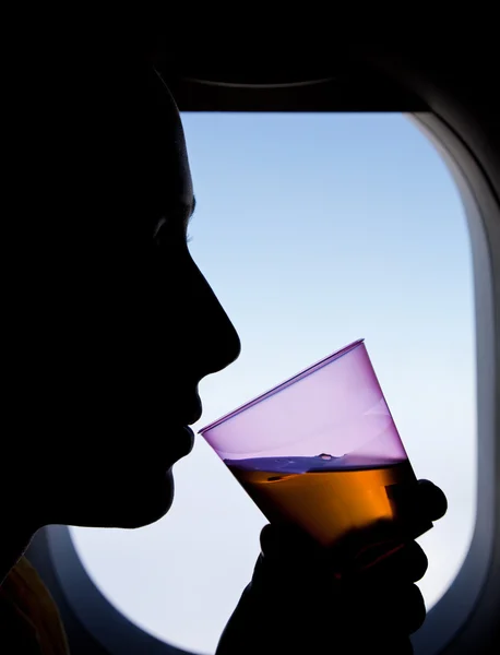 Silhouet van een vrouw passagier naast vliegtuig venster, een drank drinken. — Stockfoto