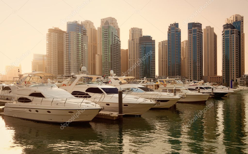 Luxurious Yachts and Boats in Front of Dubai Marina Skyscrapers, at sunset. All the logos and trade names are removed from the picture.