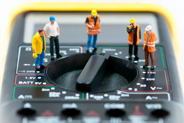 Team of miniature workers on top of multimeter. Macro photo — Stock Photo, Image