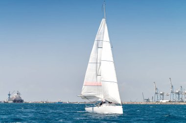 Denizde yelkenli, arka planda liman