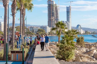 Limasol, Kıbrıs - 17 Ekim 2021: Güneşli bir günde deniz kenarında yürüyen insanlar