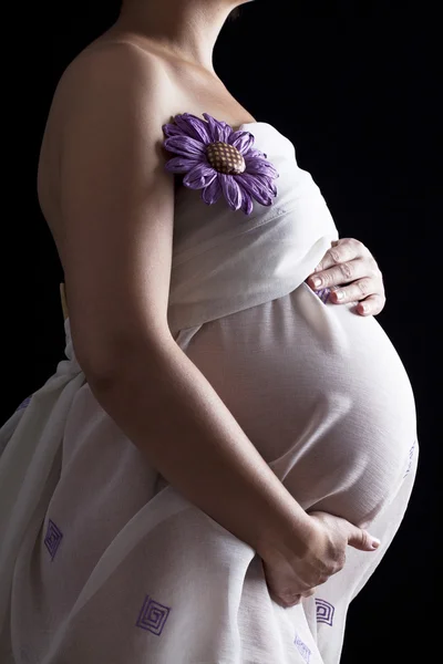 Belly of pregnant woman with pink flower on black background — Stock Photo, Image