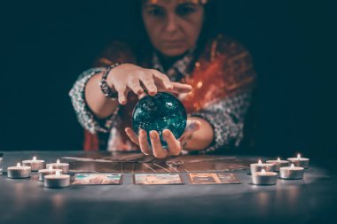 Falcı elinde mumların yanındaki masada tarot kartlarıyla. Tarot kartları kristal kürenin üzerine yayılmış. Tahmin konsepti..