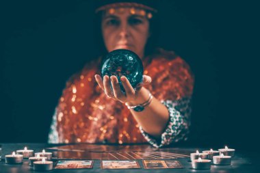 Falcı elinde mumların yanındaki masada tarot kartlarıyla. Tarot kartları kristal kürenin üzerine yayılmış. Tahmin konsepti..