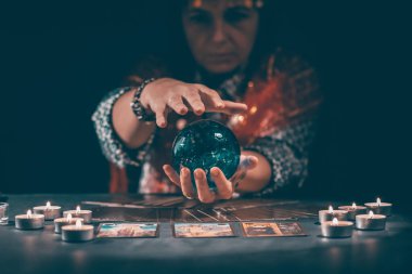 Falcı elinde mumların yanındaki masada tarot kartlarıyla. Tarot kartları kristal kürenin üzerine yayılmış. Tahmin konsepti..