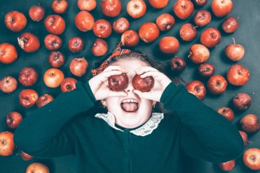 Küçük kız kırmızı elmalarla eğleniyor. Düz bir fotoğraf.