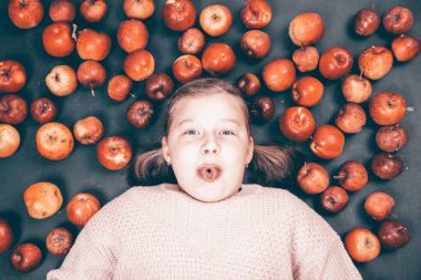 Küçük kız kırmızı elmalarla eğleniyor. Düz bir fotoğraf.