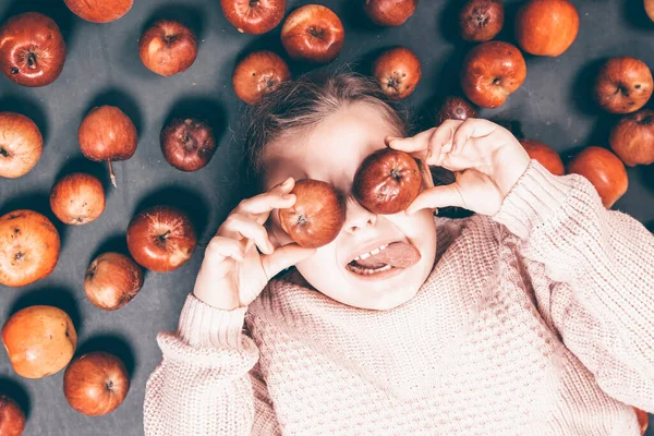 Küçük kız kırmızı elmalarla eğleniyor. Düz bir fotoğraf.