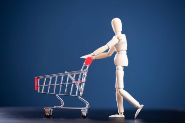 Alışveriş konseptine git. Mavi arka planda alışveriş arabası olan tahtadan bir figür.