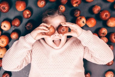 Küçük kız kırmızı elmalarla eğleniyor. Düz bir fotoğraf.