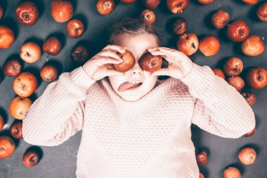 Küçük kız kırmızı elmalarla eğleniyor. Düz bir fotoğraf.