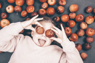 Küçük kız kırmızı elmalarla eğleniyor. Düz bir fotoğraf.