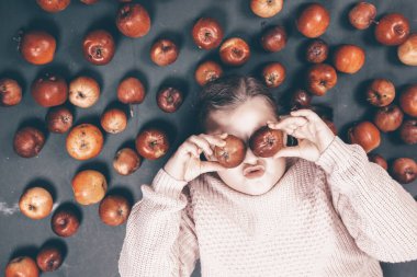 Küçük kız kırmızı elmalarla eğleniyor. Düz bir fotoğraf.