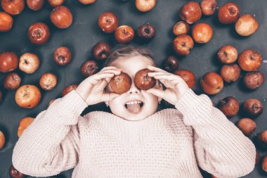 Küçük kız kırmızı elmalarla eğleniyor. Düz bir fotoğraf.