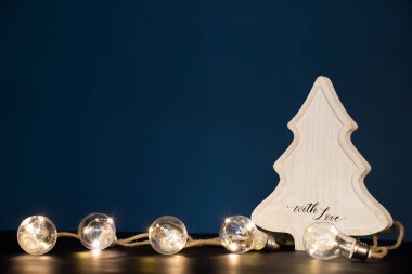 Kış, tatiller ve dekorasyon konsepti. Parlak tatil ışıkları üzerine ahşap Noel ağacı.