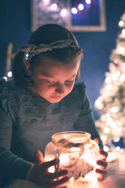 Elinde ev yapımı zencefilli kurabiyelerle şeker kavanozu tutan genç bir kız. Arka planda Noel ışıkları.