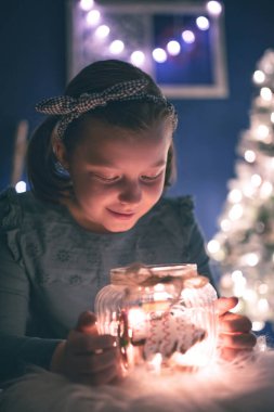 Elinde ev yapımı zencefilli kurabiyelerle şeker kavanozu tutan genç bir kız. Arka planda Noel ışıkları.