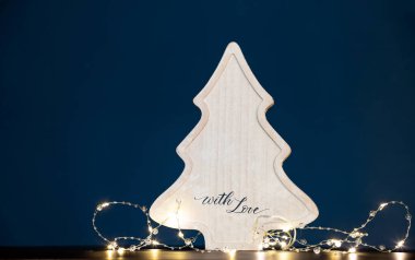 Kış, tatiller ve dekorasyon konsepti. Parlak tatil ışıkları üzerine ahşap Noel ağacı.
