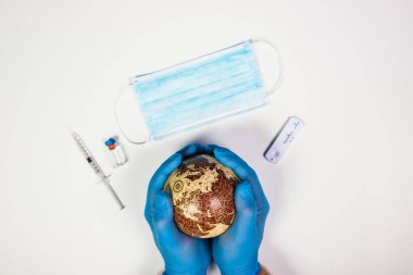 Dünya salgını tehlike kavramı. Arka planda Dünya gezegenini, aşıyı, maskeyi ve testi tutan doktorların elleri